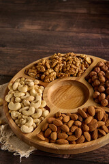 Wall Mural - Wooden round plate with various types of nuts, standing on a burlap on the table. Dried cashews, almonds, hazelnuts and walnuts are laid out on a wooden rack