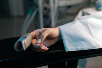 Wall Mural - Closeup cropped shot of unrecognizable female hand with pulse oximeter on finger on operating table under anesthesia operating room. Process of medical surgery. Concept of surgery and emergency.