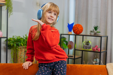 happy caucasian teenager girl kid in wireless headphones relaxing taking a break sits on couch at ho