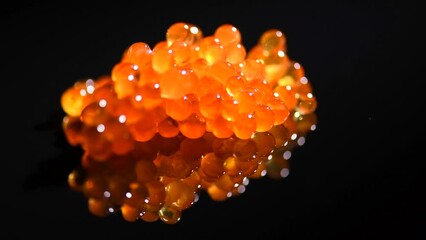 Wall Mural - Red caviar close up. Salmon caviar rotating over black background with reflection. Delicious gourmet food.  Delicatessen. Texture of caviar. Seafood, macro shot 