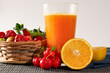 Fresh Organic Acerola and Orange Juice in a glass cup with sliced orange fruit and acerola berries in a bamboo basket in white background in front view