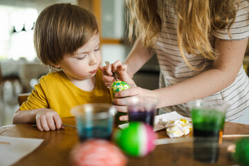 Wall Mural - Big sister and her brother dyeing Easter eggs at home. Children painting colorful eggs for Easter hunt. Kids getting ready for Easter celebration.