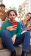 © CarlosBarquero - Diverse group of university friends sitting on street staircase, serious students people using and looking at smart phones. Photo shows addiction to new technologies and social networks, generation Z.
