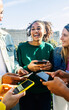 © Xavier Lorenzo - Vertical shot of happy young people using smartphone device at city street. Millennial girl enjoying social media content on cell app with diverse friends. Technology, friendship and youth concept