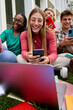 © CarlosBarquero - Vertical Group of cheerful young multiracial university student immersed on their mobile cell, technology addicted friends outside university campus. Smiling gen z people concentrated using smartphone