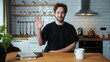 © mahirkart - A curly hair man sitting in modern kitchen at home talking to camera making conference business call