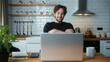 © mahirkart - Cozy curly hair man sitting in the kitchen having video call conversation through using laptop computer. Share news, talk to family, enjoy webchat virtual meeting