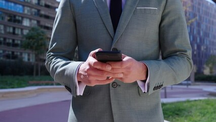 Unrecognizable caucasian professional outside modern office building using phone. Business man in formal clothes typing message browsing online on mobile. Entrepreneur consulting electronic agenda