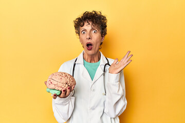 Wall Mural - Doctor holding a brain model on yellow studio surprised and shocked.