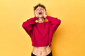 Wall Mural - Mid-aged caucasian woman on vibrant yellow laughs joyfully keeping hands on head. Happiness concept.