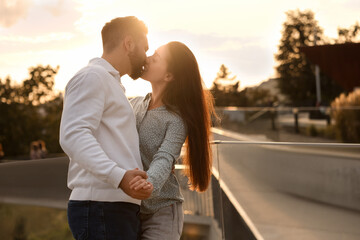 Lovely couple kissing and dancing together outdoors at sunset, space for text