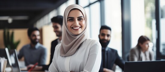 Canvas Print - Diverse young colleagues working together in a modern office. Muslim woman smiling after completing a task.