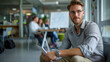 © Marta B - Professional, confident man in an office setting with a tablet in hand. In the background, there's a group of colleagues engaged in a discussion with a presentation board