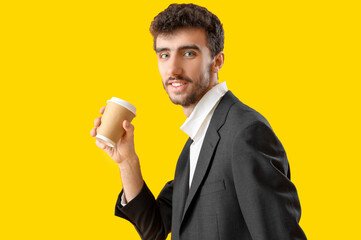 Poster - Young man in suit with cup of coffee on yellow background