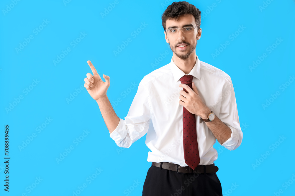 Young man in suit pointing at something on blue background