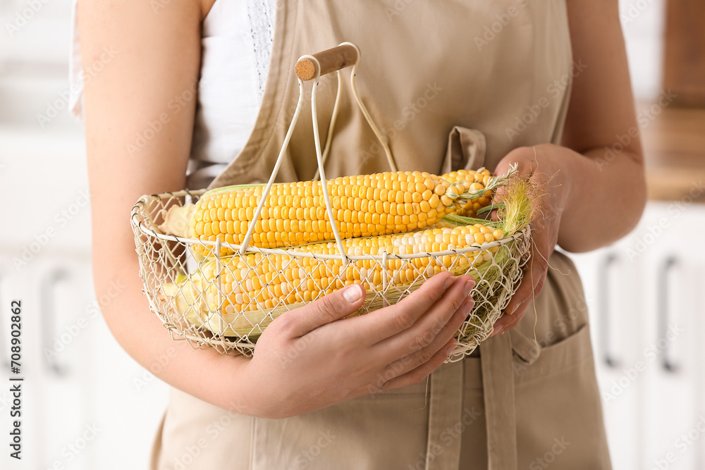 Woman holding basket with fresh corn cobs in kitchen