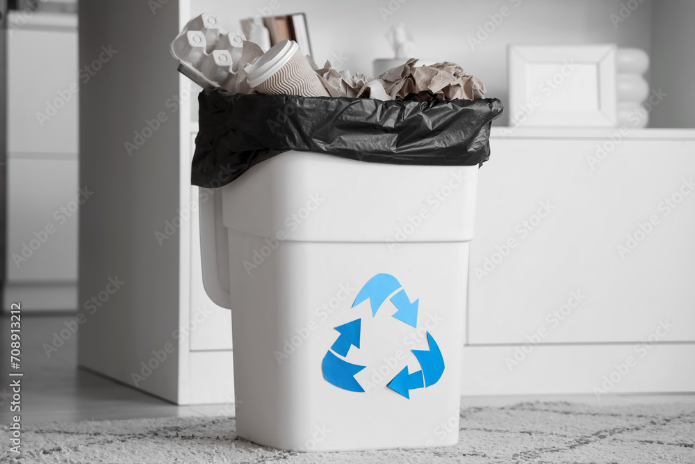 Full trash bin with different garbage and recycle logo in kitchen, closeup
