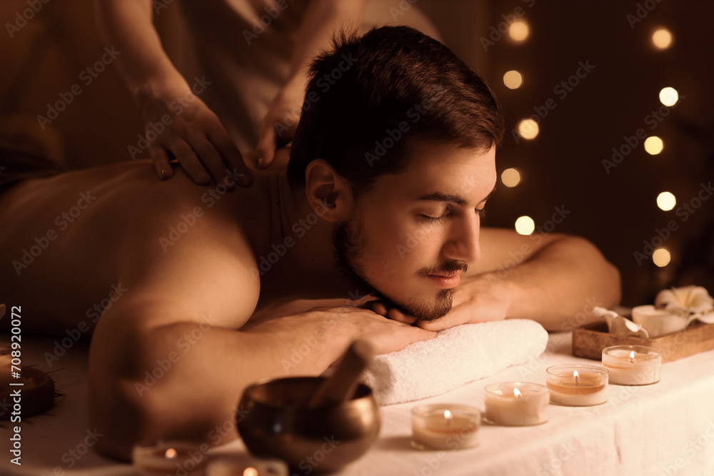 Young man getting massage in dark spa salon, closeup