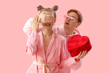 Poster - Young man surprising his beloved with gift on pink background. Valentine's Day celebration