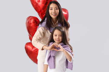 Wall Mural - Young Asian woman and her little daughter making heart with hands on white background. Valentine's day celebration