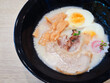 Tonkotsu ramen in a black cup topped with chashu pork, Naruto fish balls, soy-sauce pickled eggs, menma bamboo shoots and seaweed. Ramen is a distinctive Japanese style noodle soup.