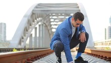 Young Man In Sunglasses Squats And Takes Stones On Railway Bridge