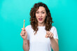 Young caucasian woman brushing teeth isolated on blue background surprised and pointing front