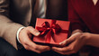 赤いリボンをかけたプレゼントを手渡しする男性と女性の手元のクローズアップ写真