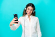 © luismolinero - Telemarketer Italian woman working with a headset isolated on blue background making a selfie