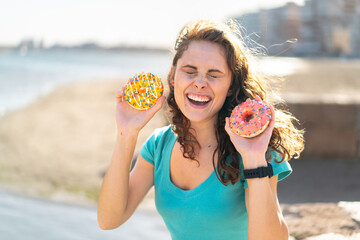 Wall Mural - Young sport woman at outdoors holding donuts with happy expression