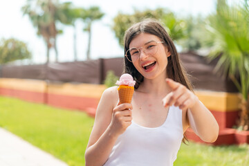 Wall Mural - Young pretty Ukrainian woman with a cornet ice cream at outdoors points finger at you with a confident expression