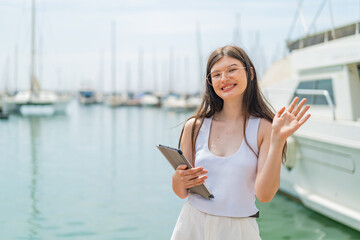 Wall Mural - Young pretty Ukrainian woman holding a tablet at outdoors saluting with hand with happy expression