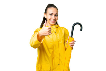 Wall Mural - Young Arabian woman with rainproof coat and umbrella over isolated chroma key background with thumbs up because something good has happened