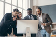 © gstockstudio - Group of confident business people looking at computer monitor while having meeting in the office