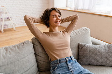 Wall Mural - pretty young woman realxing at home sitting on sofa, smiling, happy, free time