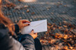 © Andrew - Woman opens a white envelope with a letter. Autumn foliage in the background.