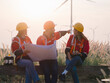 Group of maintenance engineers preparing and planning inspection of wind turbines, holding tablets, looking at wind turbines