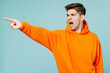 Young mad dissatisfied displeased man he wears orange hoody casual clothes point index finger aside scream isolated on plain pastel light blue cyan color background studio portrait. Lifestyle concept.