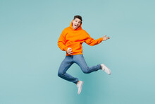 Full Body Happy Singer Young Man He Wears Orange Hoody Casual Clothes Jump High Play Do Air Guitar Gesture Isolated On Plain Pastel Light Blue Cyan Color Background Studio Portrait. Lifestyle Concept.