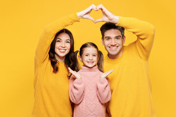 Wall Mural - Young parents mom dad with child kid girl 7-8 years old wear pink knitted sweater casual clothes hold folded hands above head like house roof isolated on plain yellow background. Family day concept.