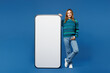 © ViDi Studio - Full body young woman in knitted sweater casual clothes big huge blank screen mobile cell phone smartphone with workspace copy space mockup area looking camera isolated on plain blue cyan background