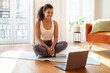 © Prostock-studio - Happy woman looking at laptop sitting on fitness mat indoors