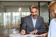 © Stock 4 You - Lawyer or real estate agent make consultation for client. Mature Latin business man and European business woman discussing project on laptop sitting at table in office. Business people work together.