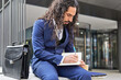 © ADDICTIVE STOCK - Mid-adult Latin businessman with long hair writing in a notebook, seated outdoors near a business briefcase