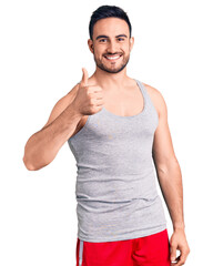 Canvas Print - Young handsome man wearing swimwear and sleeveless t-shirt doing happy thumbs up gesture with hand. approving expression looking at the camera showing success.