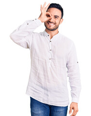 Wall Mural - Young handsome man wearing casual clothes smiling happy doing ok sign with hand on eye looking through fingers