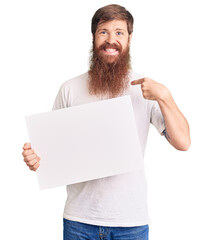 Wall Mural - Handsome young red head man with long beard holding blank empty banner pointing finger to one self smiling happy and proud