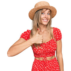 Poster - Beautiful caucasian woman wearing summer hat doing happy thumbs up gesture with hand. approving expression looking at the camera showing success.