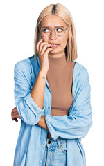 Sticker - Beautiful young blonde woman wearing glasses looking stressed and nervous with hands on mouth biting nails. anxiety problem.