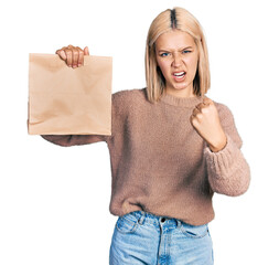 Wall Mural - Beautiful young blonde woman holding take away paper bag annoyed and frustrated shouting with anger, yelling crazy with anger and hand raised